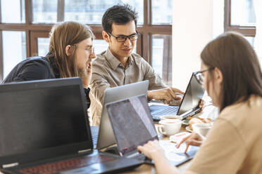 Programmers discussing over laptop near businesswoman working at startup - EVKF00096