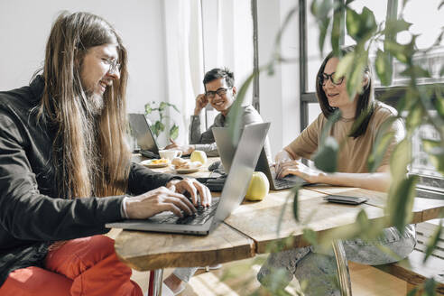 Ein Team von IT-Technikern sitzt am Tisch und programmiert an Laptops im Büro - EVKF00107