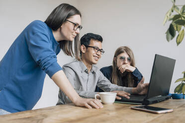 Smiling programmer discussing coding on laptop with colleagues at startup - EVKF00108