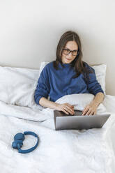 Lächelnder Programmierer, der zu Hause auf dem Bett sitzend mit seinem Laptop programmiert - EVKF00122