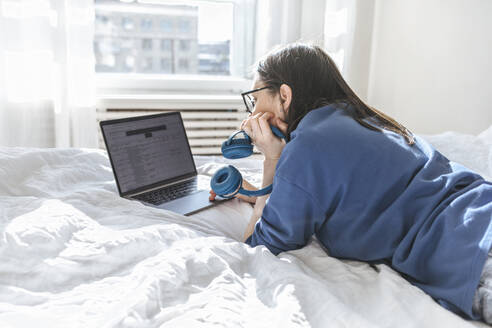 Programmierer mit Laptop auf dem Bett liegend zu Hause - EVKF00123