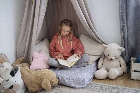 Girl with pigtails reading book in gray canopy at home - NJAF00823