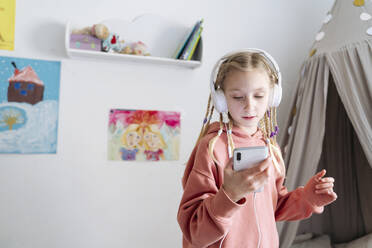 Girl listening music through headphones using smart phone at home - NJAF00842