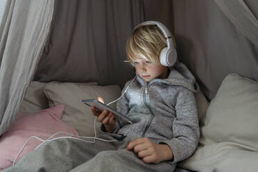 Boy wearing headphones using smart phone in canopy at home - NJAF00844