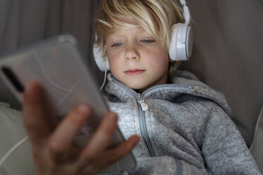Junge mit Kopfhörern, der zu Hause das Internet über sein Smartphone nutzt - NJAF00845