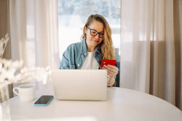Smiling woman holding credit card near laptop at home - OLRF00223