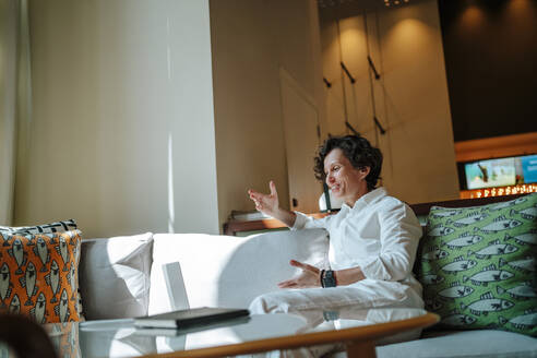 Lächelnde Geschäftsfrau bei einem Videogespräch über einen Laptop in der Hotellobby - MDOF01889