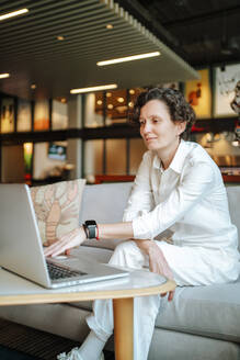 Selbstbewusste Geschäftsfrau mit Laptop auf dem Sofa in der Lobby eines Hotels - MDOF01900