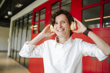 Glückliche Frau mit drahtlosen Kopfhörern, die in der Hotellobby Musik hört - MDOF01920