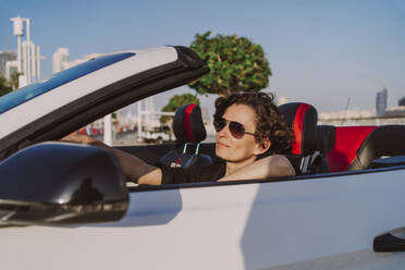 Lächelnde Frau mit Sonnenbrille in weißem Cabrio an einem sonnigen Tag - MDOF01930