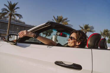 Reife Frau sitzt in einem weißen Cabrio an einem sonnigen Tag - MDOF01931