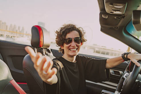 Glückliche Frau mit Sonnenbrille gestikuliert im Cabrio an einem sonnigen Tag - MDOF01934