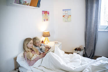 Blonder Bruder und blonde Schwester lesen ein Buch auf dem Bett zu Hause - NJAF00854