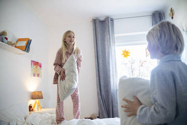 Geschwister spielen mit Kissen im Schlafzimmer zu Hause - NJAF00856