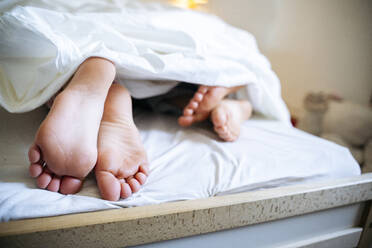 Siblings feet looking from blanket on bed at home - NJAF00863