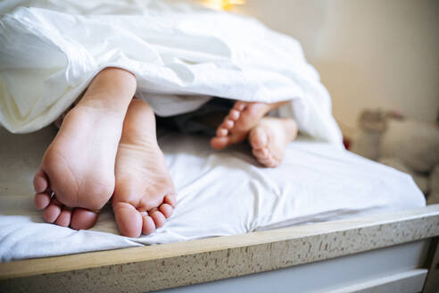 Geschwister Füße schauen von Decke auf Bett zu Hause - NJAF00863