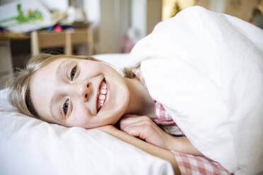 Lächelndes Mädchen, das auf einem Kissen im Bett zu Hause liegt - NJAF00866