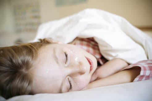 Mädchen schläft auf einem Bett mit Decke zu Hause - NJAF00867