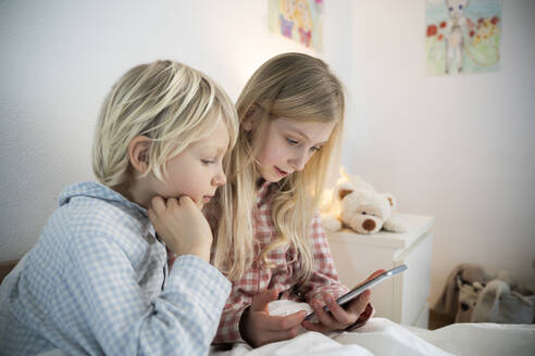 Sister using smart phone sitting with brother at home - NJAF00875