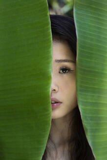 Young woman hiding behind banana leaves - EAF00139