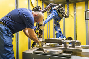 Wartungsingenieur bei der Arbeit mit einem blauen Roboterarm in einer modernen Fabrik - AAZF01706
