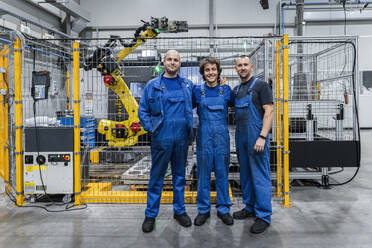 Smiling technician colleagues in front of machinery with robotic arm at modern factory - AAZF01710