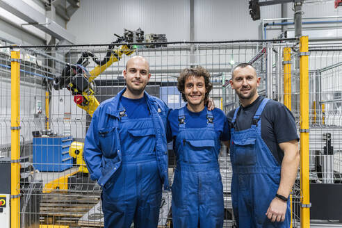 Smiling engineering colleagues in front of machinery with robotic arm at modern factory - AAZF01711