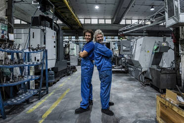 Smiling technicians standing back to back with arms crossed in industry - AAZF01717