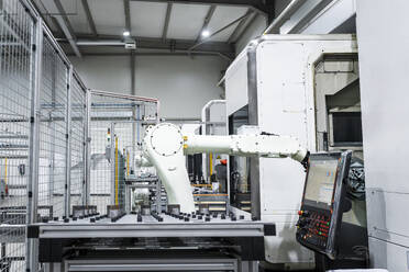 White robotic arm by CNC machinery in modern factory building - AAZF01723