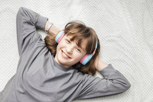 Smiling girl listening to music with hands behind head at home - ELMF00102