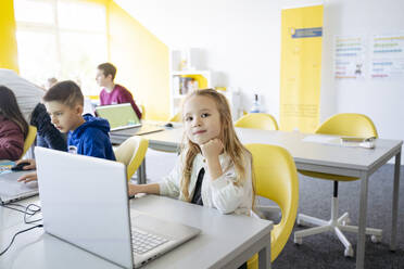 Mädchen sitzt mit der Hand am Kinn und benutzt einen Laptop in einem Computer-Klassenzimmer in der Schule - NJAF00882