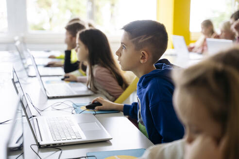 Engagierter Junge mit Laptop lernt im Klassenzimmer Computerprogrammierung - NJAF00891