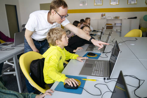 Professor zeigt auf Laptop und unterrichtet Junge im Klassenzimmer im Programmieren - NJAF00892