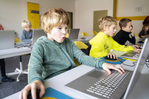 Blond boy using laptop learning computer programming at desk - NJAF00897