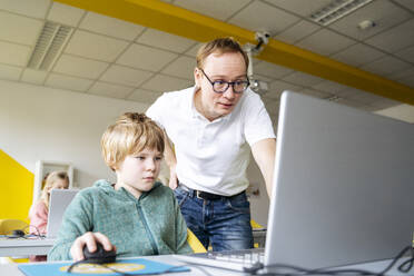 Professor hilft einem Jungen bei der Codierung im Laptop am Schreibtisch - NJAF00900