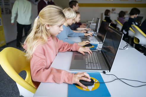 Engagiertes blondes Mädchen mit Laptop Lerncomputer am Schreibtisch im Klassenzimmer - NJAF00903