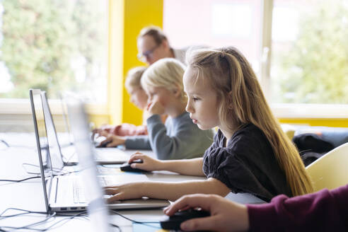 Blondes Mädchen mit Laptop beim Lernen von Computerprogrammierung im Klassenzimmer - NJAF00906