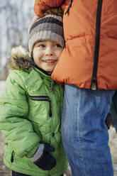 Lächelnder Junge mit Strickmütze, stehend mit Vater im Winter - ANAF02744