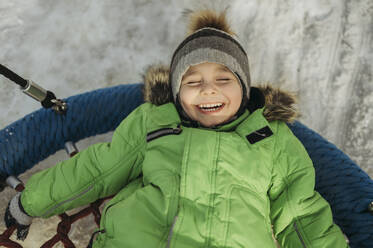 Unbekümmerter Junge auf einer Schaukel im Winter im Park liegend - ANAF02749