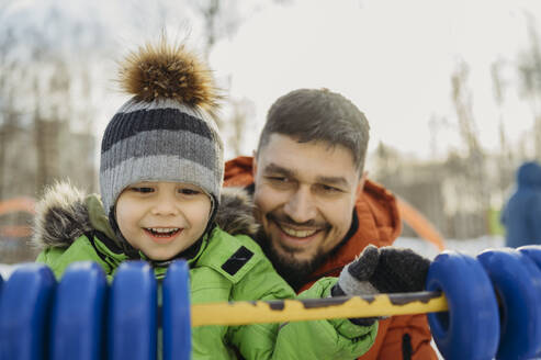 Lächelnder Mann spielt mit seinem Sohn im Park im Winter - ANAF02755