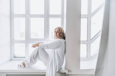 Mature woman sitting on window sill at home - ADF00296