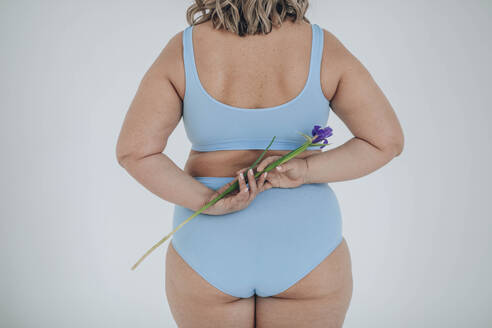 Üppige Frau versteckt blaue Irisblüte vor weißem Hintergrund - ADF00299