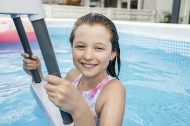 Smiling girl holding ladder in swimming pool - ELMF00106