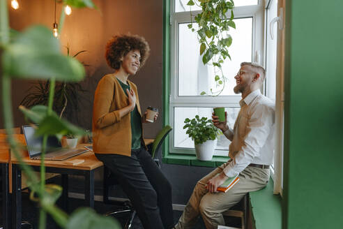 Smiling multiracial businessman and businesswoman with disposable cups discussing in coworking office - YTF02004
