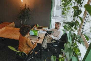 Geschäftskollegen, die an einem Schreibtisch sitzen und in einem Coworking Space über Strategien diskutieren - YTF02005