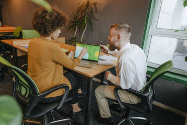 Gemischtrassige Geschäftskollegen diskutieren über einem Laptop am Schreibtisch in einem Coworking-Büro - YTF02012