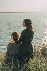 Tochter und Mutter schauen an einem sonnigen Tag aufs Meer - ADF00305