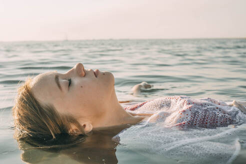 Carefree teenage girl floating on water in sea - ADF00308