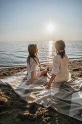 Mother and daughter sitting on blanket at beach - ADF00309