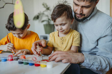 Vater mit Kindern, die Ostereier aus Pappe bemalen - ANAF02767